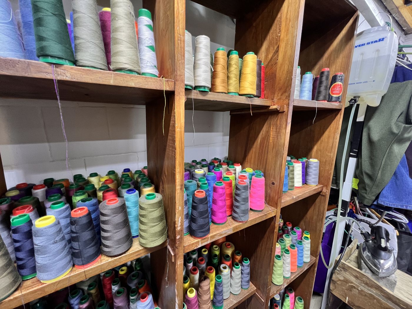 Detalle de carretes de hilo de distintos colores ordenados en la estantería de madera